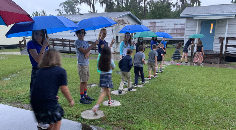 Middle school students holding umbrellas for elementary school students walking to class
