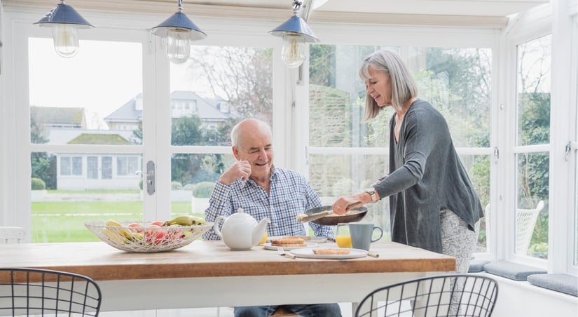 a grey haired couple eating breakfast in a sunny sunroom